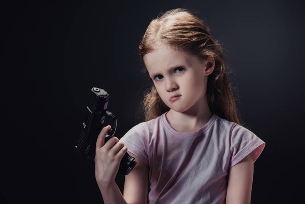 offended child holding gun and looking at camera isolated on black - Foto, immagini