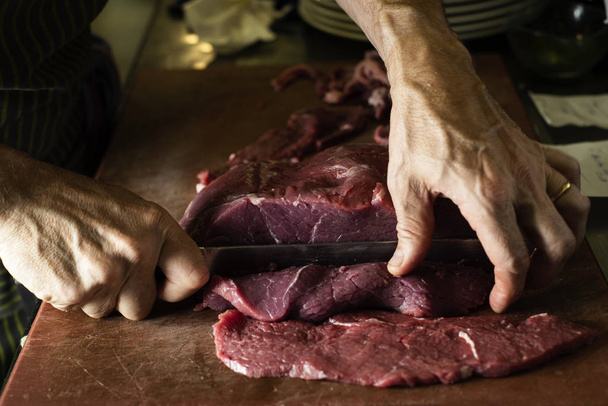 άνθρωπος κοπή ένα κομμάτι του βοείου κρέατος σε μια επαγγελματική κουζίνα - Φωτογραφία, εικόνα