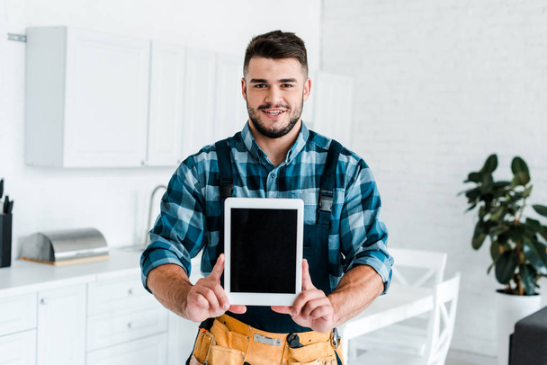 happy handyman holding digital tablet with blank screen  - Foto, afbeelding