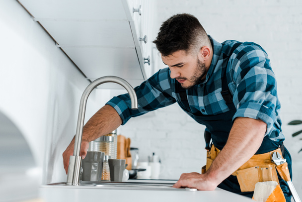 selective focus of handsome handyman working near sink in kitchen  - Photo, Image