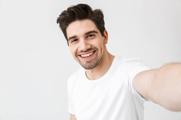 Excited happy young man posing isolated over white wall background make a selfie by camera. - Fotó, kép