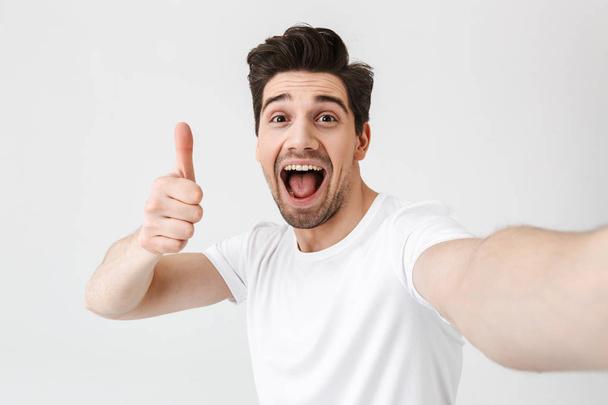 Excited happy young man posing isolated over white wall background make a selfie by camera. - Фото, зображення