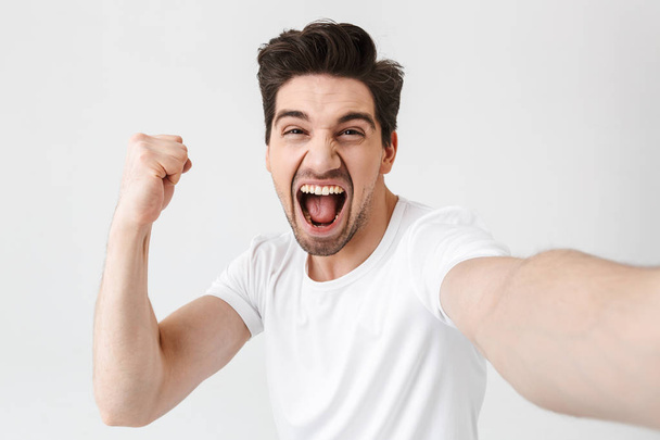 Excited happy young man posing isolated over white wall background make a selfie by camera. - Φωτογραφία, εικόνα