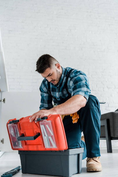 handsome repairman looking at opened toolbox in kitchen  - Foto, imagen
