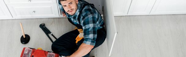 tiro panorâmico de handyman barbudo sentado no chão perto da caixa de ferramentas
  - Foto, Imagem