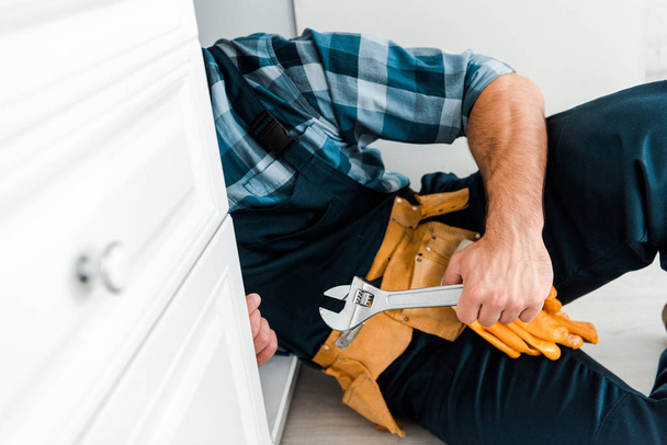 cropped view of handyman holding adjustable wrench near kitchen cabinet  - Φωτογραφία, εικόνα
