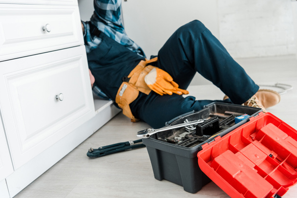 selective focus of repairman working near kitchen cabinet and toolbox - Foto, imagen