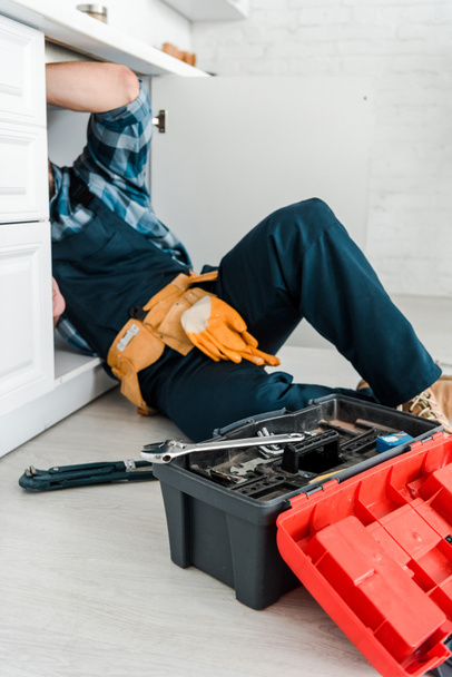 Ausgeschnittene Ansicht eines Reparateurs, der in der Nähe von Küchenschrank und Werkzeugkiste arbeitet - Foto, Bild