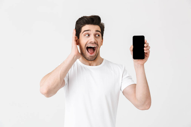 Excited happy young man posing isolated over white wall background showing display of mobile phone. - Fotoğraf, Görsel