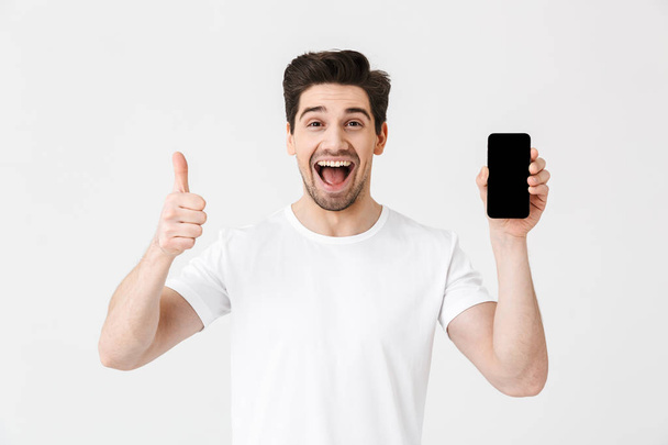 Excited happy young man posing isolated over white wall background showing display of mobile phone. - Foto, afbeelding