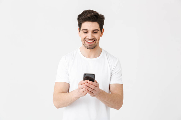 Excited happy young man posing isolated over white wall background using mobile phone. - Fotó, kép