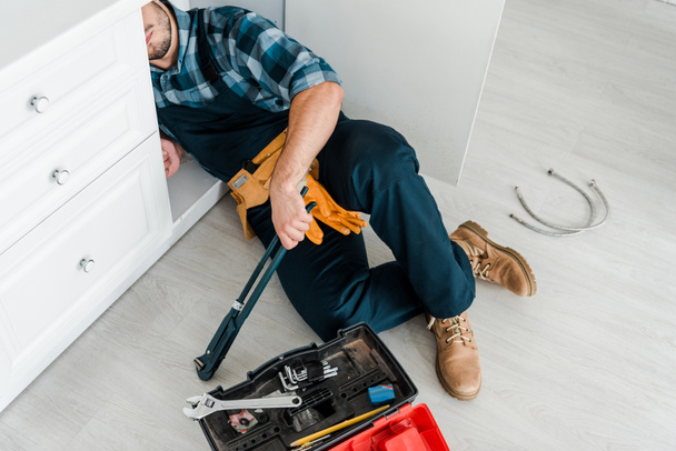 обрезанный вид бородатого ремонтника, работающего возле кухонного шкафа и ящика с инструментами
 - Фото, изображение