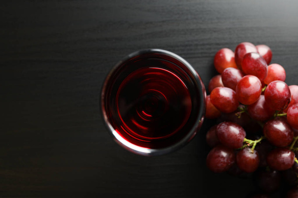 Winogrona i szkło z winem na ciemnym stole, widok z góry - Zdjęcie, obraz
