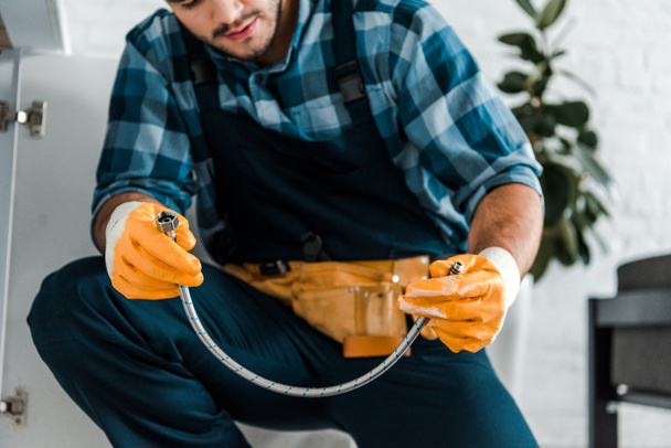 cropped view of bearded repairman holding metal hose  - Fotó, kép