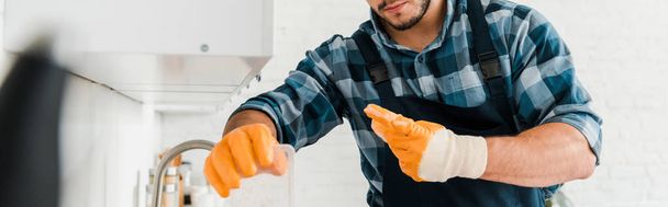 panoramic shot of handyman in rubber gloves standing in kitchen  - Fotografie, Obrázek