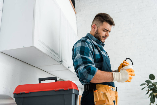 handsome bearded man holding funnel near toolbox in kitchen  - Photo, Image