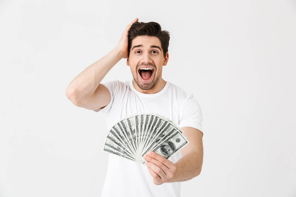 Shocked excited happy young man posing isolated over white wall background holding money. - Foto, Imagem