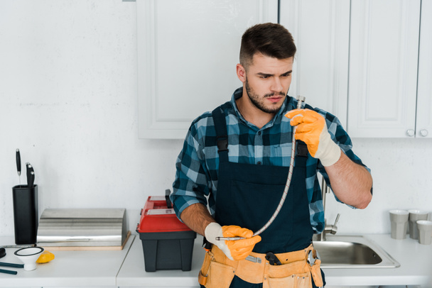 bearded  repairman in rubber gloves looking at metal hose  - Фото, зображення
