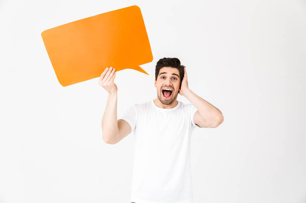 Emotional excited young man posing isolated over white wall background holding speech bubble. - Фото, зображення