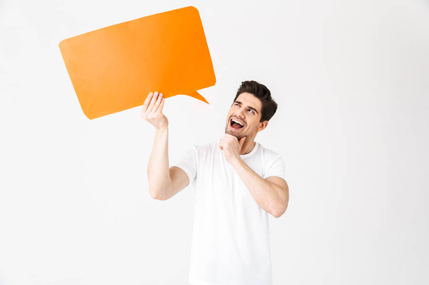 Emotional excited young man posing isolated over white wall background holding speech bubble. - Photo, Image