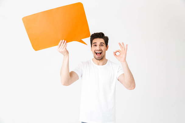 Emotional excited young man posing isolated over white wall background holding speech bubble. - Foto, immagini