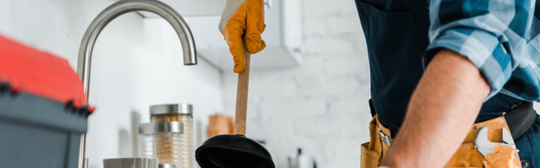 панорамный снимок мастера, держащего вантуз на кухне
  - Фото, изображение