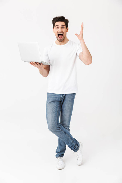 Schockierter aufgeregter junger Mann posiert isoliert mit Laptop über weißer Wand. - Foto, Bild
