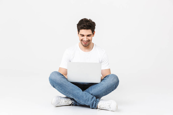 Excited young man posing isolated over white wall using laptop computer. - Foto, afbeelding