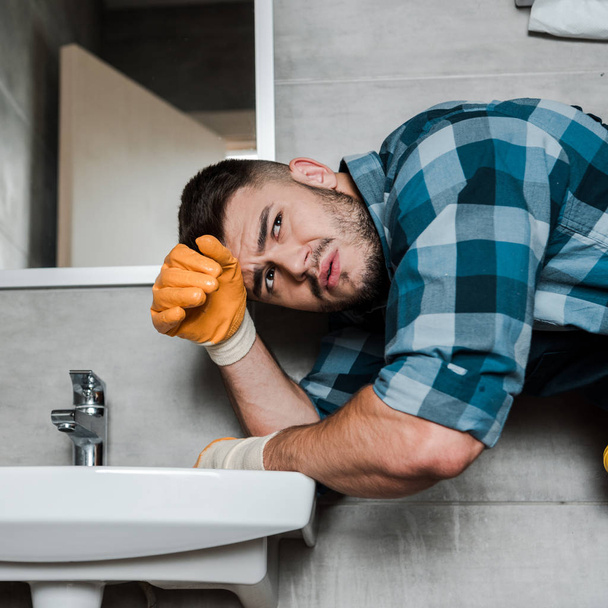 handsome bearded handyman standing near sink in bathroom  - Фото, зображення