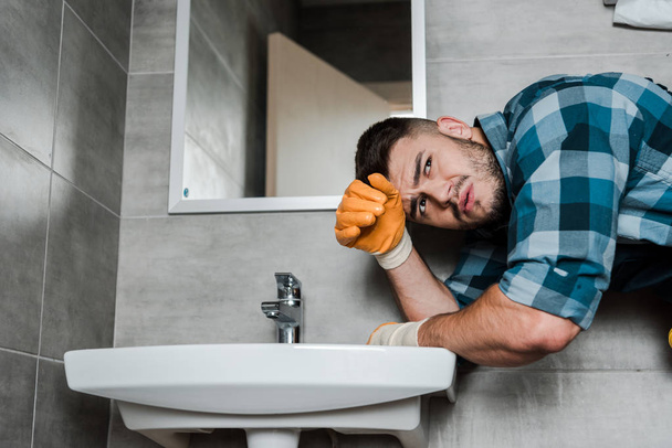 pohledný vousatý opravák stojící blízko dřezu v koupelně  - Fotografie, Obrázek