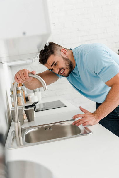 selective focus of stressed man touching faucet in kitchen  - Фото, зображення