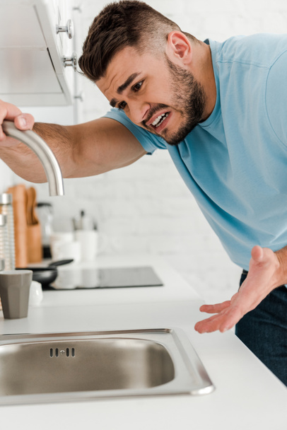 stressed man touching faucet and gesturing in kitchen  - Фото, зображення