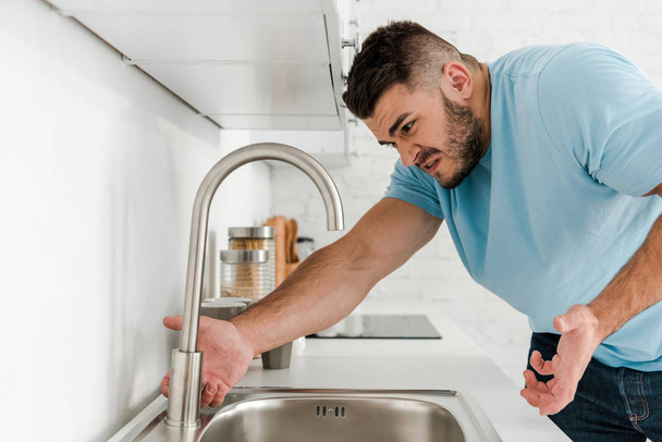 angry man gesturing near faucet in kitchen  - Foto, afbeelding