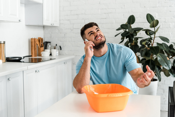 angry bearded man talking on smartphone near plastic wash bowl  - Foto, afbeelding