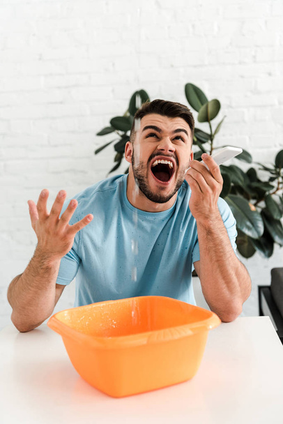 selectieve focus van boos bebaarde man schreeuwen terwijl kijken naar water gieten in plastic Wash Bowl  - Foto, afbeelding