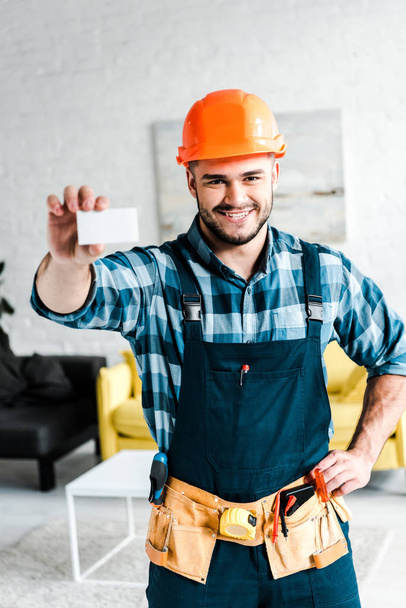 happy worker holding blank card and standing with hand on hip  - Photo, Image