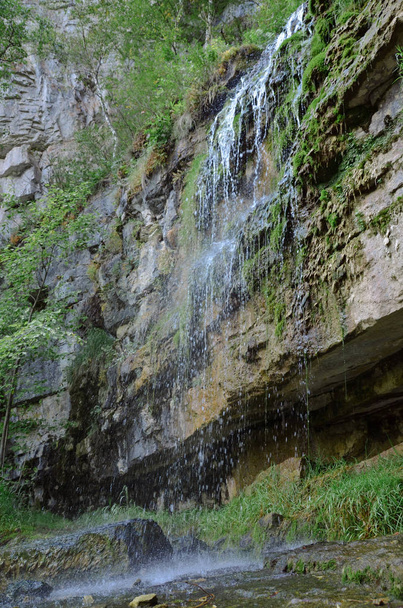Нижний вид на крутую скалу, покрытую мхом с водопадом из чистого источника
 - Фото, изображение