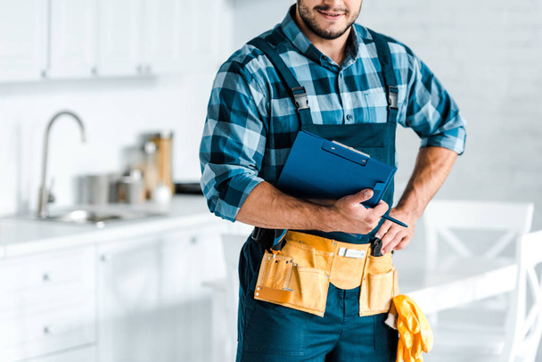 cropped view of bearded workman standing with hand on hip and holding clipboard  - Photo, Image