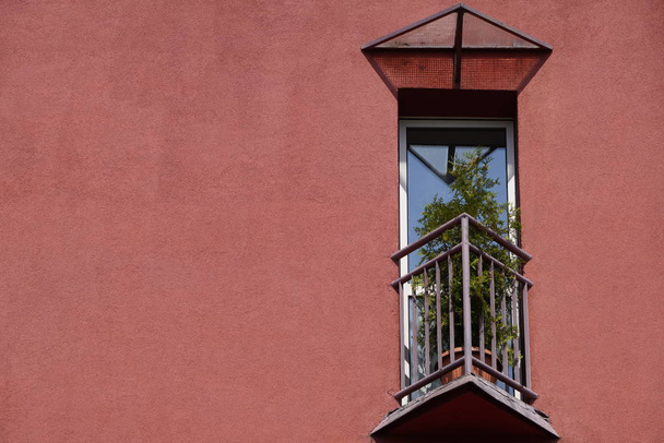 небольшой треугольный балкон в доме с коралловым фасадом и цветами в горшке на заборе. место для отдыха души
 - Фото, изображение