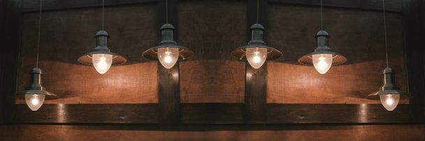 Gloeiende retro lampen hangen op een bruine houten achtergrond. - Foto, afbeelding