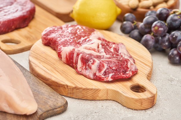 Raw mmeat tenderloin on wooden cutting board near grapes and lemon on marble surface - Photo, Image