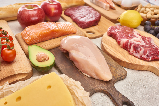 Friss nyers baromfi, hús, hal az alma, citrom, sajt, Cseresznyeparadicsom és az avokádó felének közelében lévő fa vágódeszkán - Fotó, kép