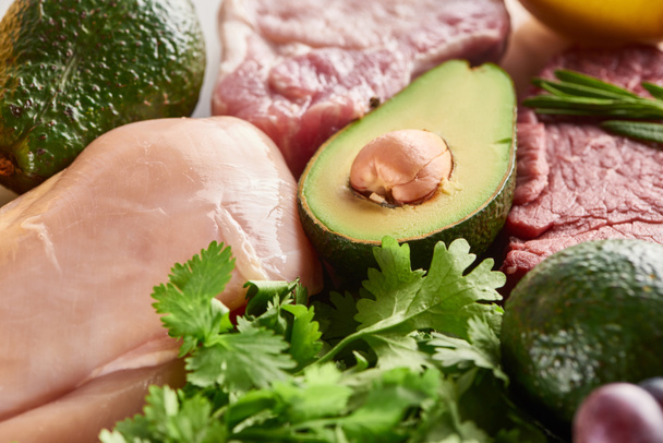 Close up view of half of avocado between raw meat and poultry with parsley twigs - Photo, Image