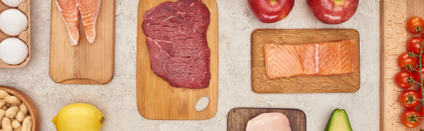 Панорамный снимок деревянных досок с мясом и рыбой возле овощей на мраморной поверхности
 - Фото, изображение