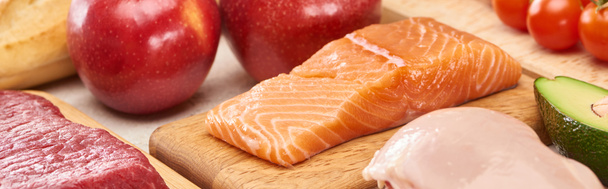 Панорамний знімок сирого лосося біля м'яса, птиці та овочів на дерев'яних обробних дошках
 - Фото, зображення