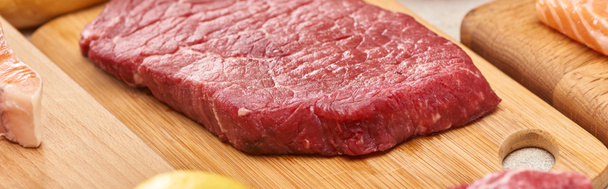 Panoramic shot of raw meat steak on wooden cutting board - Foto, afbeelding