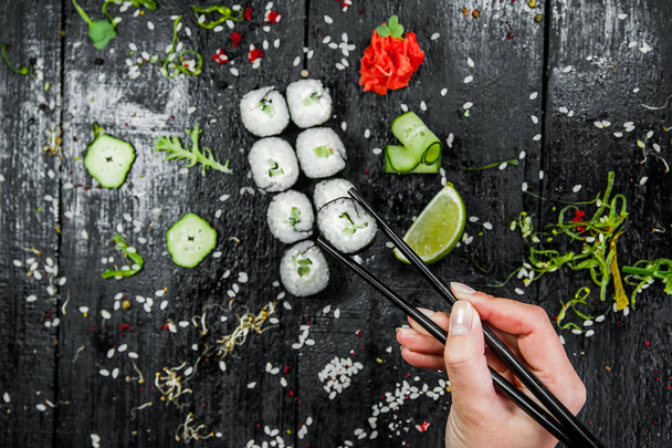 Суши в руке с палочками для еды на темном фоне
 - Фото, изображение