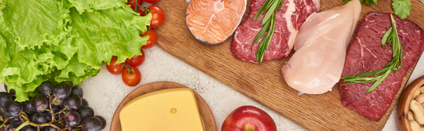 Panoraama laukaus puinen leikkuulauta raaka kala, liha ja siipikarja lähellä tomaatit, salaatti, juusto ja omena marmori pinnalla
 - Valokuva, kuva