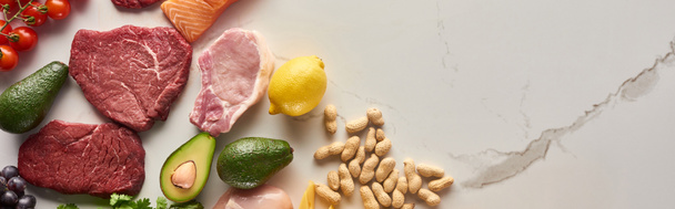 Panoramic shot of raw meat steak near avocados, lemon, peanuts on marble surface with copy space - Photo, Image