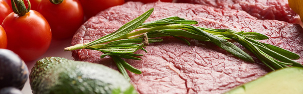 Panoramic shot of raw near steak with rosemary twig on it near cherry tomatoes - Фото, изображение